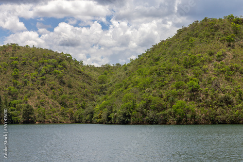 Tranquil lake of green waters with mountains covered by vegetation and blue sky with many clouds in the background
