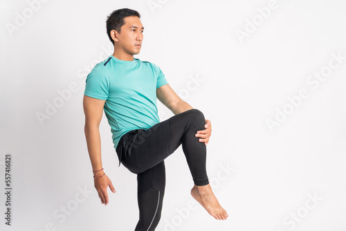asian man standing stretching legs by holding one leg forward in isolated background