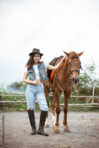 attractive asian cowboy girl standing beside horse on outdoor background