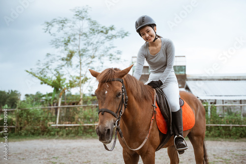 Female equestrian smiling while riding horse and holding reins in outdoor background © Odua Images