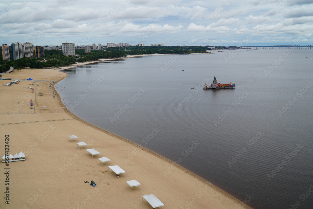 The beach on the Amazon River. On the river a ship full of Christmas decorations with nativity scene and Jesus figures and huge Christmas tree. Ponta Negra district of Manaus, Brazil. The beach on the Amazon River. On the river a ship full of Christmas decorations with nativity scene and Jesus figures and huge Christmas tree. Ponta Negra district of Manaus, Brazil.