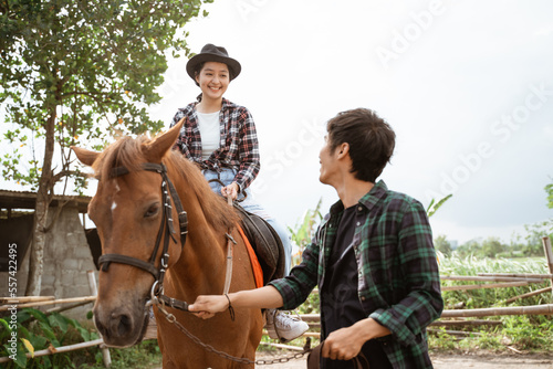 woman in cowboy hat sitting on a horse with a man holding the reins leading the horse on the ranch