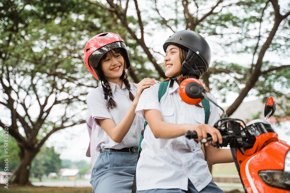 Two student girls wearing helmets chatting while riding a motorcycle together Two student girls wearing helmets chatting while riding a motorcycle together