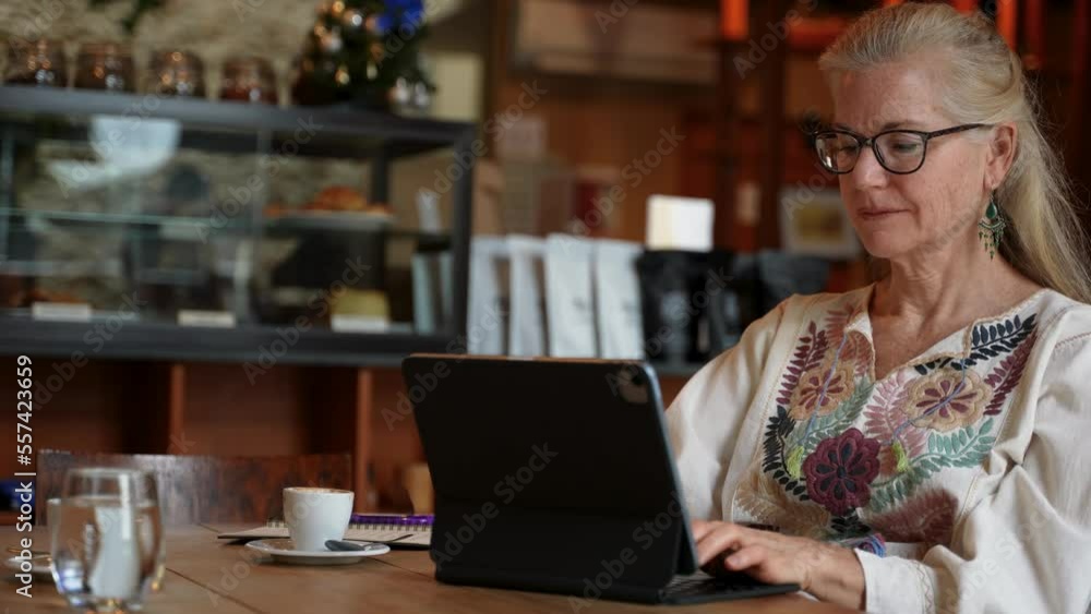 Smiling mature elderly woman typing on her laptop tablet computer wearing ethnic clothes while in a cafe coffee shop. Smiling mature elderly woman typing on her laptop tablet computer wearing ethnic clothes while in a cafe coffee shop.