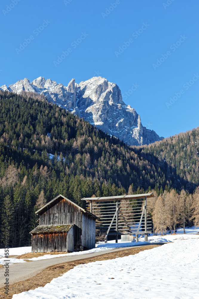 Wooden hut and harp for drying grain and the snow covered mountain peaks of the Sesto Dolomites in Winter. Alps, South Tyrol, Alto Adige, Italy, Europe