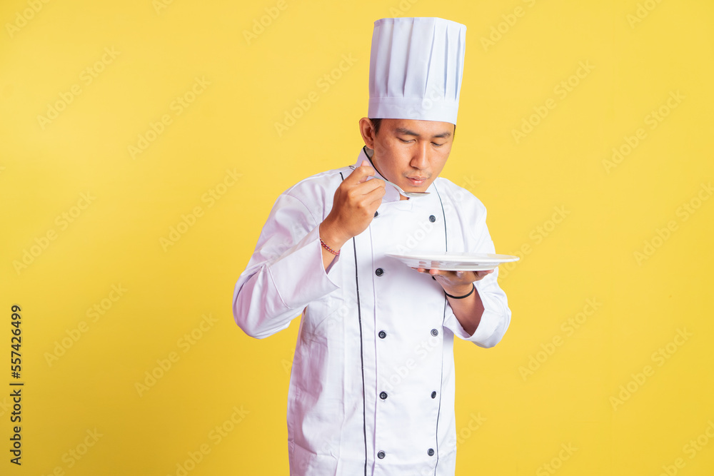 male chef tasting food with cooking spoon while holding empty serving plate on isolated background male chef tasting food with cooking spoon while holding empty serving plate on isolated background