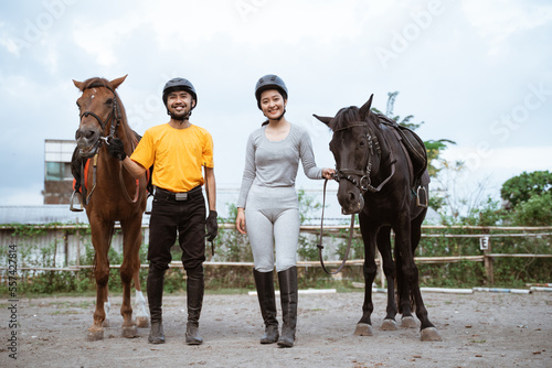 Two equestrian athletes wearing gear standing next to their horses on the field background