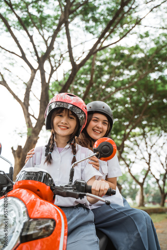 Two beautiful students wearing helmets smiling while riding a motorbike on the road © Odua Images
