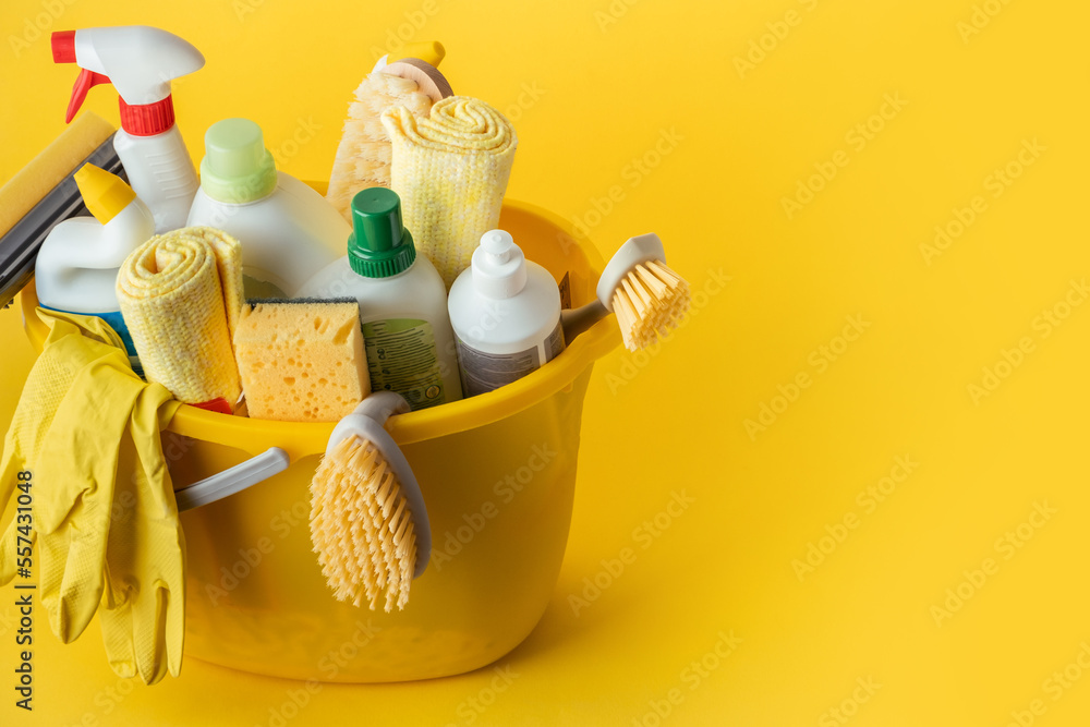 Brushes, bottles with cleaning liquids, sponges, rag and yellow rubber gloves on the yellow background. Cleaning supplies in the yellow bucket. Service of cleaning company advertisement Brushes, bottles with cleaning liquids, sponges, rag and yellow rubber gloves on the yellow background. Cleaning supplies in the yellow bucket. Service of cleaning company advertisement