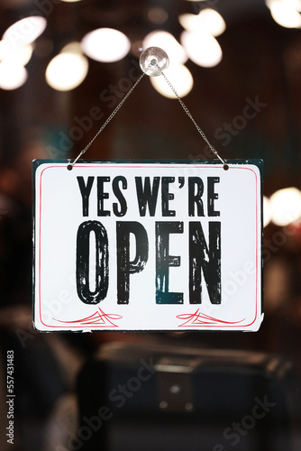 Inscription Yes we're open metal plate with black and white sign on glass door store, cafe, beautystore, barbershop after coronavirus lockdown quarantine. business reopen again photo