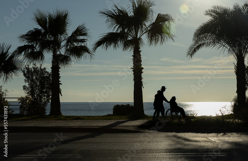 Fotografía silhouettes of people carrying an elderly man in a wheelchair against the backdrop of a sunset