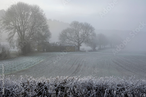 Beautiful Wintry landscape in English countryside at dawn with thick fog hiding farm buildings across the fields photo