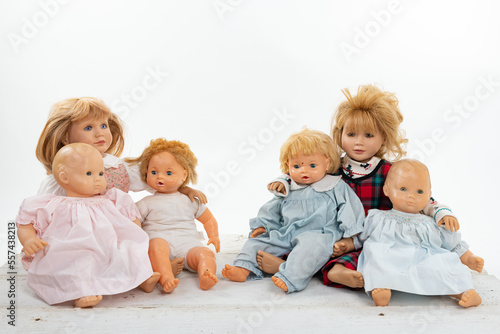 Canvas-taulu Collection of multiple dolls sitting on a rough white wooden table isolated on w