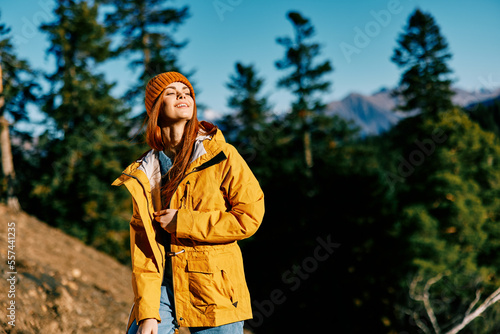 Woman red hair on a hike in the mountains walking a smile and look at the view of nature autumn in a yellow cape and cap full-length happiness