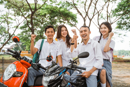 Happy high school students with clenched fists celebrating graduation on motorbike