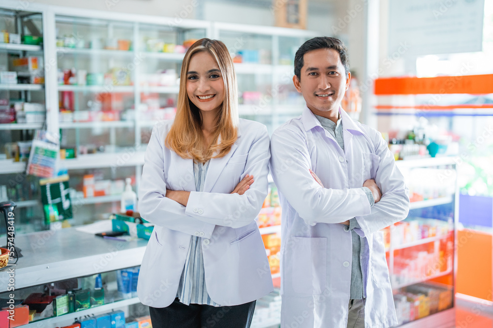 Two asian female and male pharmacists standing smiling at the pharmacy