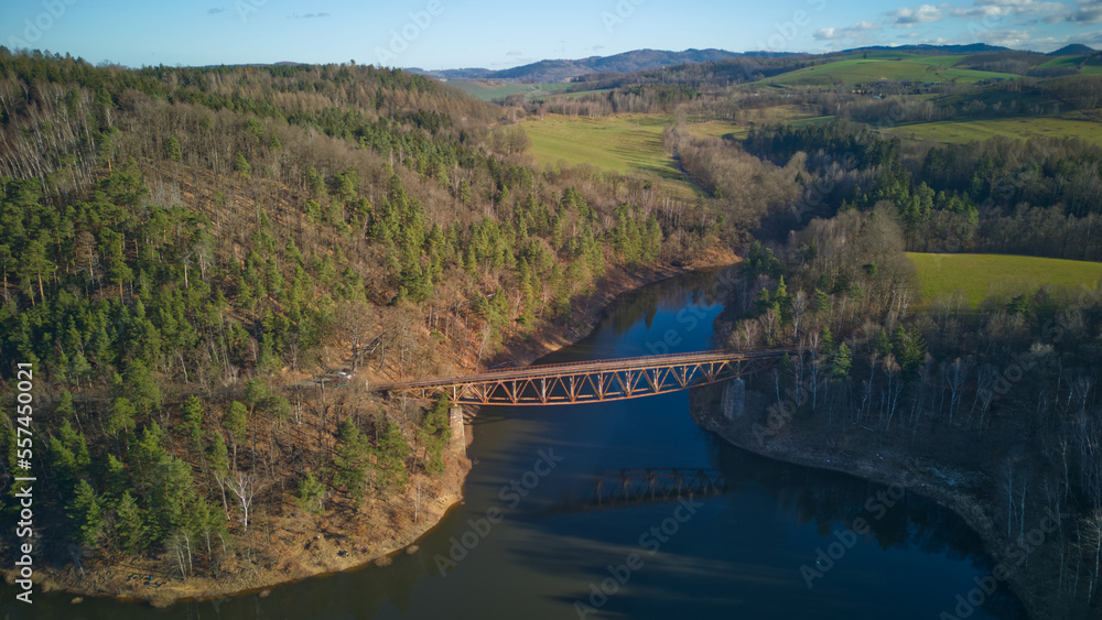 Aerial view of steel underspanned suspension railway bridge over Bobr River in Pilchowice, Wonderfull lake with islands and green forests in mountains on a early spring day in Pilchowice, Poland