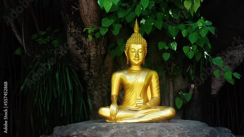 A closeup of a sitting on a stone golden Buddha statue in a garden with a green leaves background. 