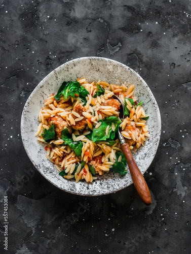 Orzo pasta with meatballs and spinach in tomato sauce on a dark background, top view