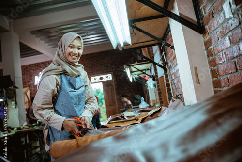 Craftwoman smiling while cutting on table in leather fabric in studio