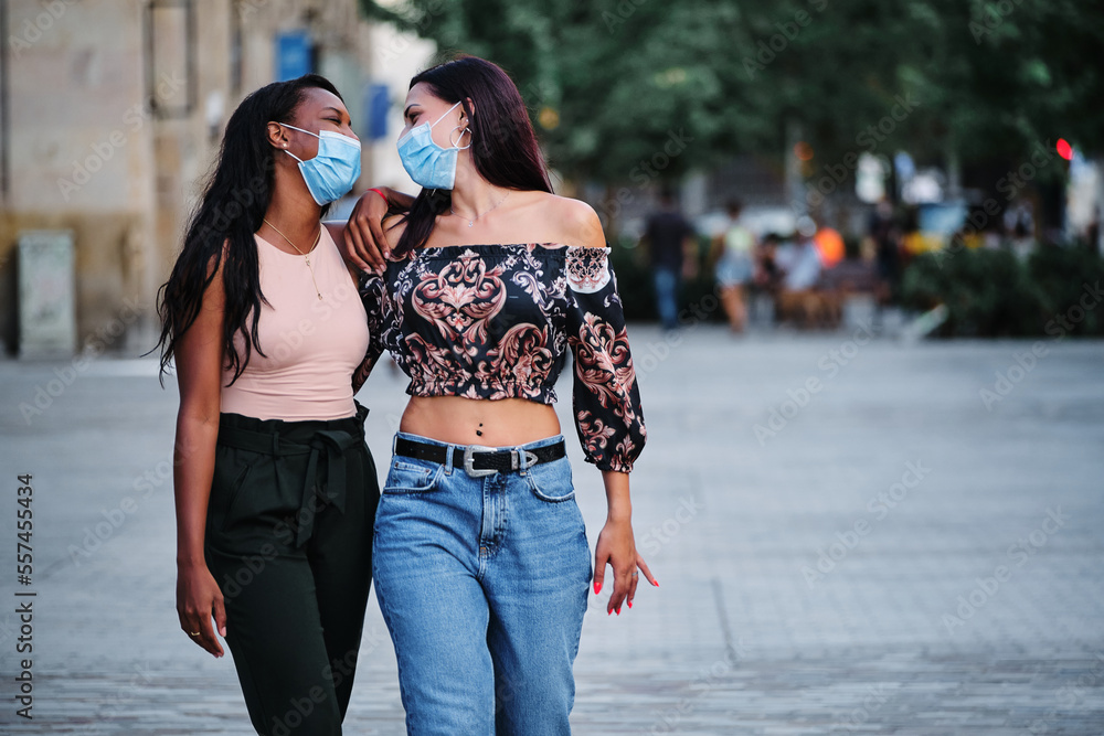 Lesbian couple embracing while walking in the street with protective mask