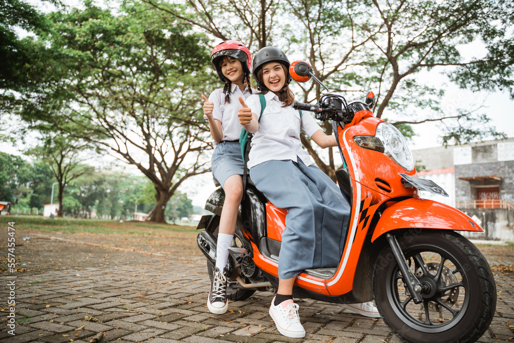 Obraz premium Bottom view of two student girls wearing helmets with thumbs up while riding a motorcycle together