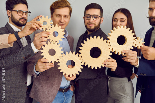 Group of business people connecting wooden cogwheels together. Office colleagues joining gears in chain. Collaboration, teamwork, professional corporate interaction and cooperation concept