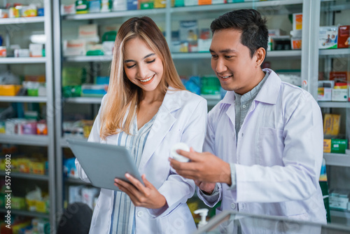 female pharmacist working with male pharmacist checking medicine with a list on the pad at the pharmacy