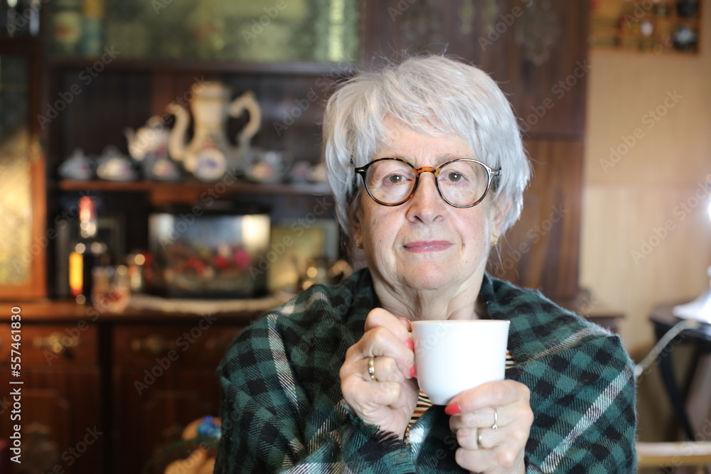 Senior woman covered in a blanket holding warm drink Senior woman covered in a blanket holding warm drink