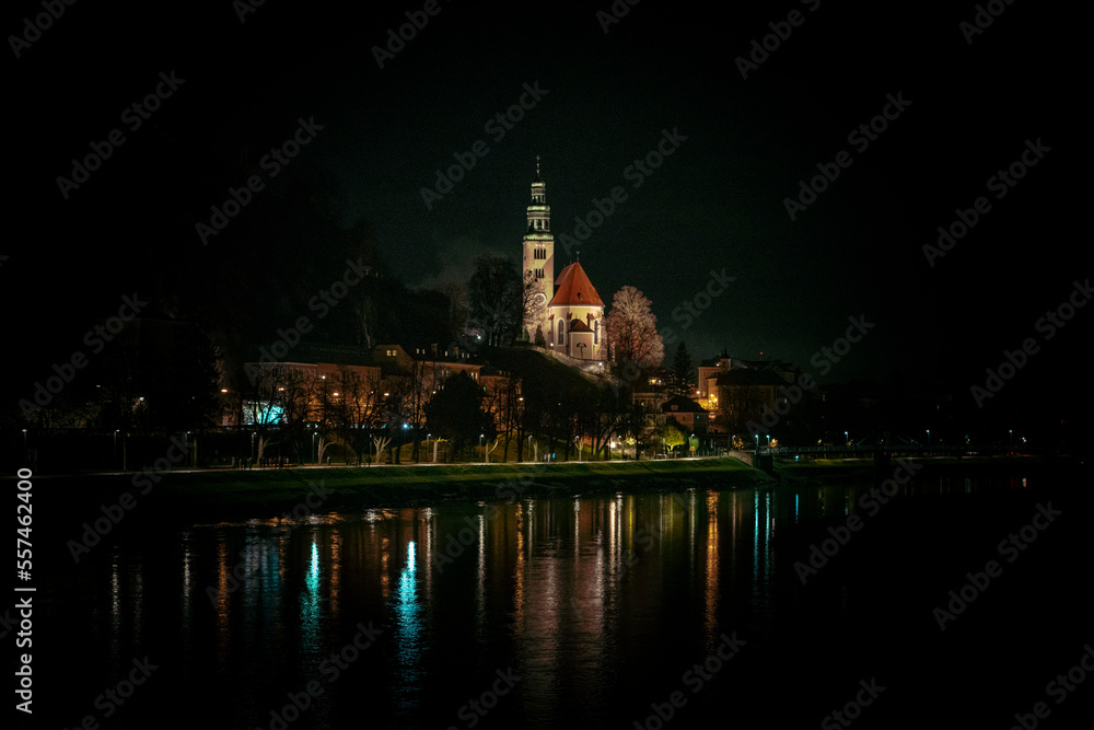 Müllner Church in Salzburg, Austria, at night with lights from the banks of the Salzach river