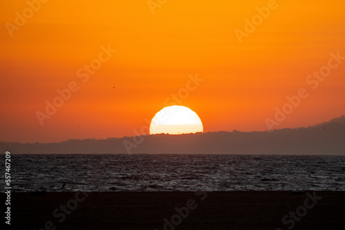 Scenic and tranquil view of seascape and beautiful bright sun setting down behind silhouette mountain with orange sky in background at Los Angeles © Aerial Film Studio