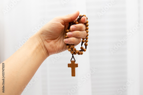 Hand holding a wooden rosary with a crucifix at the end. Pray on the rosary