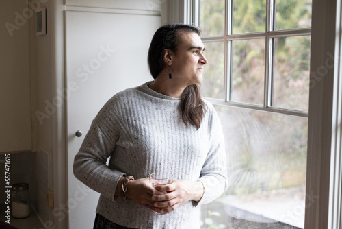 Non-binary person smiling and looking out of the window.