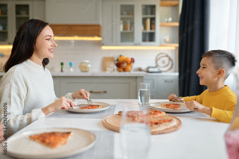 Young mother and cute little son eating pizza at home