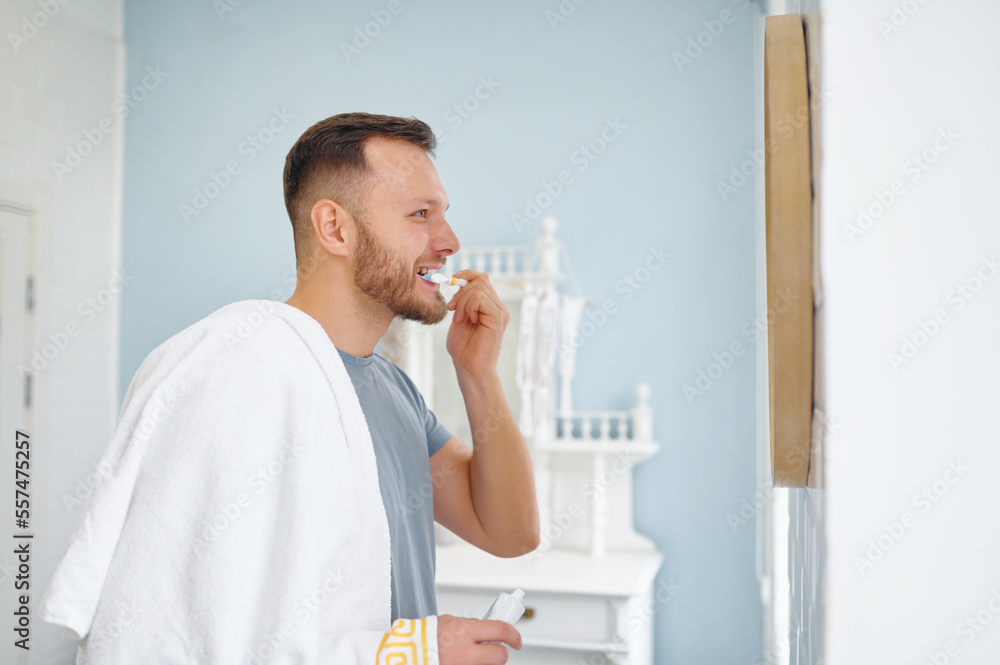 Man brushing teeth in bathroom looking at mirror side view shot Man brushing teeth in bathroom looking at mirror side view shot