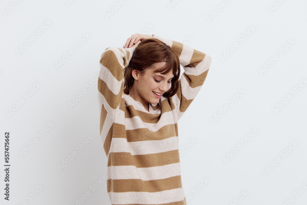 horizontal photo on a light background of a pleasant, beautiful, attractive woman straightening her hair standing in a stylish striped sweater sideways to the camera horizontal photo on a light background of a pleasant, beautiful, attractive woman straightening her hair standing in a stylish striped sweater sideways to the camera