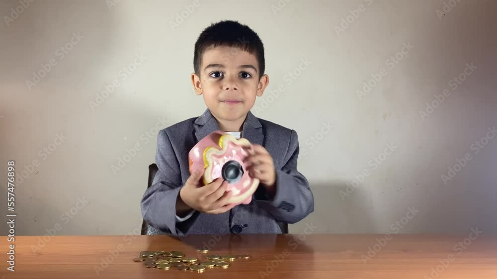 Preschool boy in a suit shaking a piggy bank with a smile. Kids savings concept. High quality 4k footage