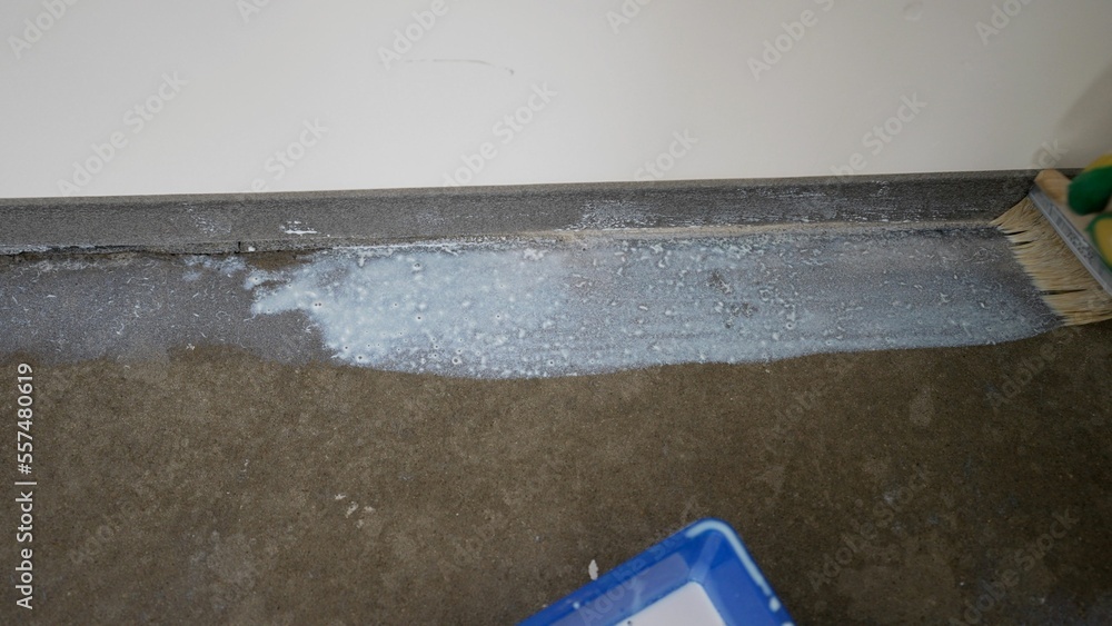 Naklejka premium Grounding the floor, preparing the floor for laying mortar. A worker applies a primer to the floor with a brush.