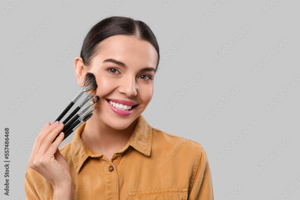 Happy woman with different makeup brushes on light grey background, space for text Happy woman with different makeup brushes on light grey background, space for text