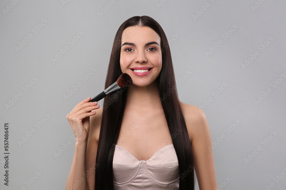 Fototapeta premium Happy woman applying makeup on light grey background
