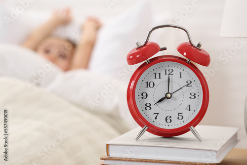 Cute little girl awaking in cosy bed, focus on alarm clock