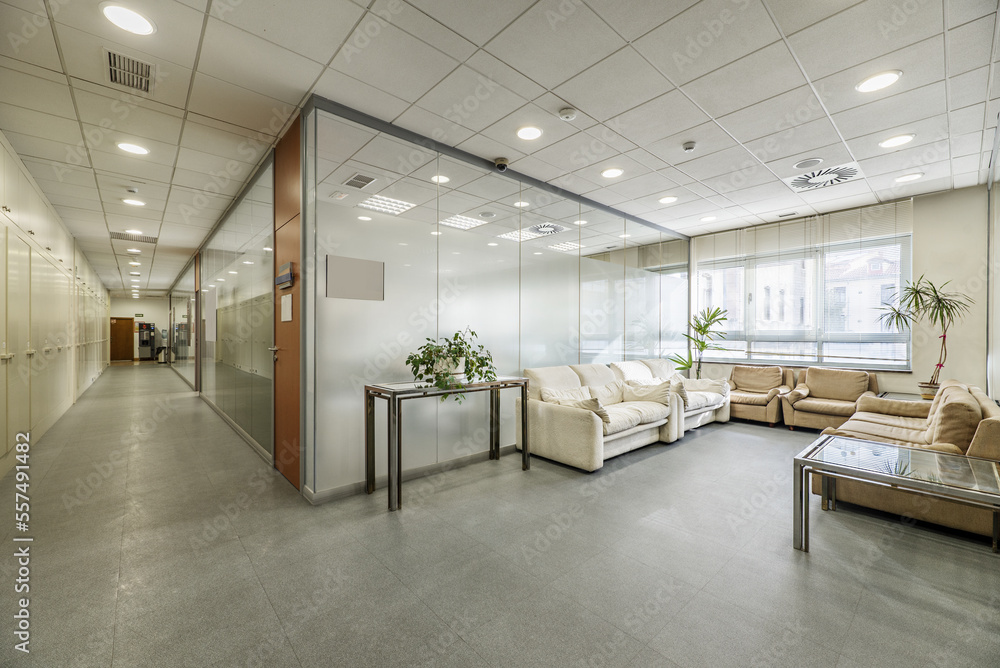 Corridor of an office building and separate offices with glass partitions, waiting areas with sofas and technical ceilings