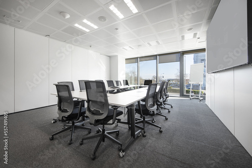 long white boardroom table with black swivel chairs on gray carpet floor with windows in background
