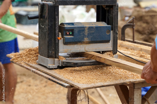 A carpenter is using a thickness planer to roll a sheet of wood to have a consistent thickness to be suitable for woodworking. Soft and selective focus.