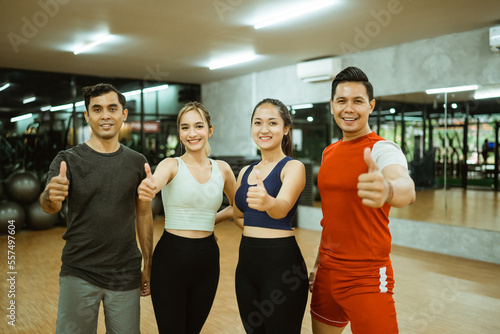 Group of diverse young friends in sportswear standing with thumbs up during break in gym