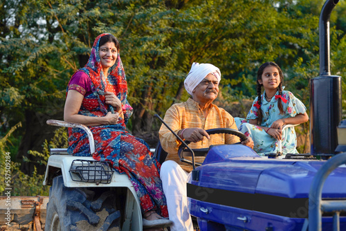 Indian farmer family sitting on tractor at field.