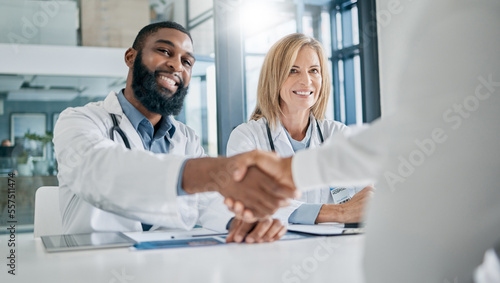 Handshake, partnership or happy doctors in a meeting after successful medical surgery or reaching healthcare goals. Teamwork, woman or black man smiles shaking hands with a worker in hospital office