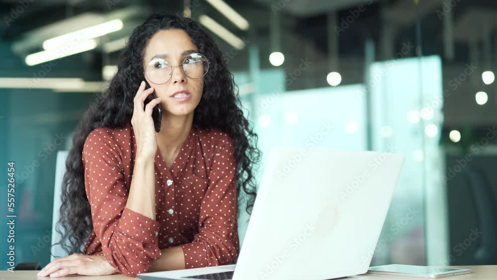 confident busy attractive business woman employee talking on the cell phone sitting in modern office at the computer desk at workplace indoors curly dark haired brunette female speaks conversation confident busy attractive business woman employee talking on the cell phone sitting in modern office at the computer desk at workplace indoors curly dark haired brunette female speaks conversation