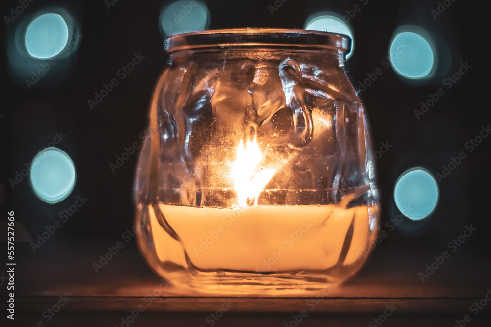 Closeup glass jar with burning candle placed on table at dark night at home Closeup glass jar with burning candle placed on table at dark night at home