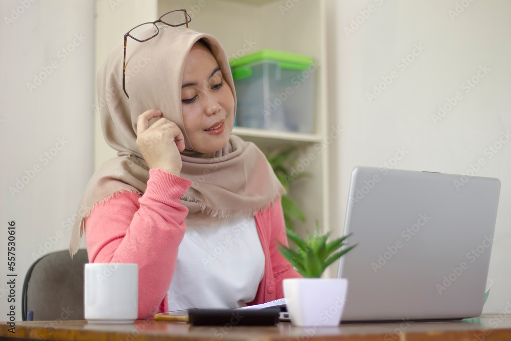asian business woman in hijab drinking coffee while sitting at table with laptop asian business woman in hijab drinking coffee while sitting at table with laptop
